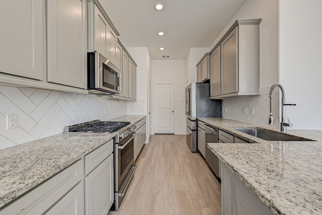 kitchen with decorative backsplash, appliances with stainless steel finishes, light wood-type flooring, sink, and light stone counters