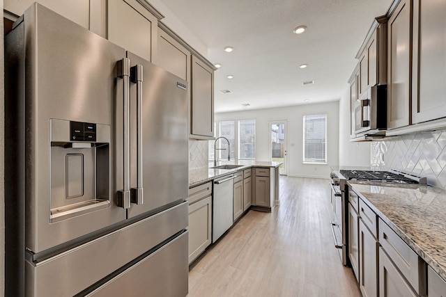 kitchen featuring light stone countertops, sink, light hardwood / wood-style floors, decorative backsplash, and high end appliances