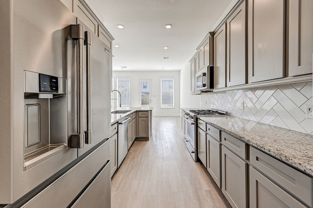 kitchen with decorative backsplash, light hardwood / wood-style flooring, sink, light stone countertops, and premium appliances