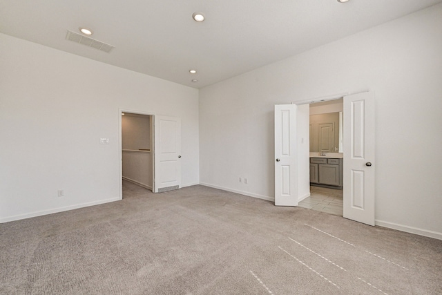 unfurnished bedroom with ensuite bath, a walk in closet, and light colored carpet