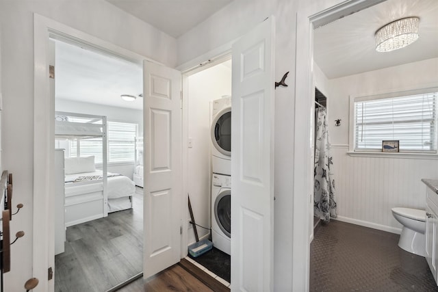 laundry room with a wealth of natural light, wooden walls, dark hardwood / wood-style flooring, and stacked washing maching and dryer