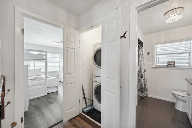 clothes washing area with stacked washer / drying machine, dark wood-style flooring, and laundry area
