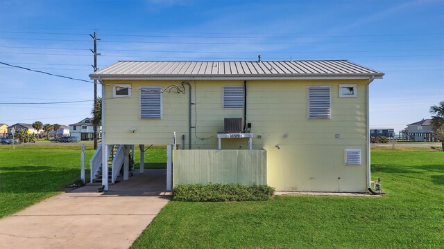 rear view of house with driveway, a yard, and metal roof