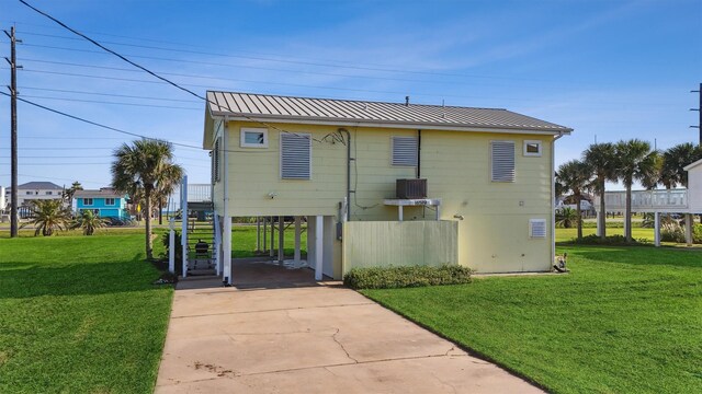 rear view of house featuring metal roof, a yard, concrete driveway, and stairway