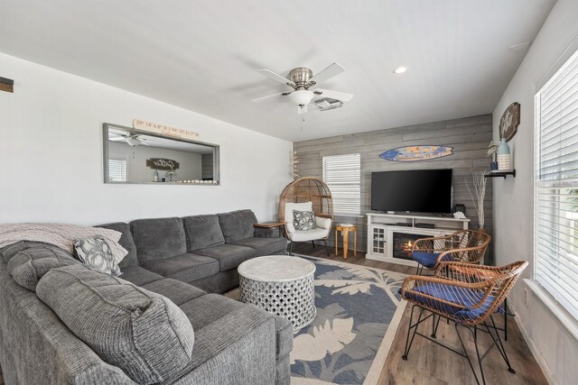 living room with an accent wall, recessed lighting, a ceiling fan, wood walls, and wood finished floors