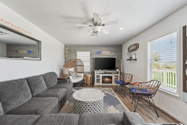 living room with light hardwood / wood-style floors, a wealth of natural light, wooden walls, and ceiling fan