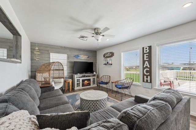 living room featuring ceiling fan, hardwood / wood-style flooring, wooden walls, and a fireplace