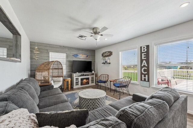 living room with a ceiling fan, an accent wall, wood finished floors, a lit fireplace, and recessed lighting
