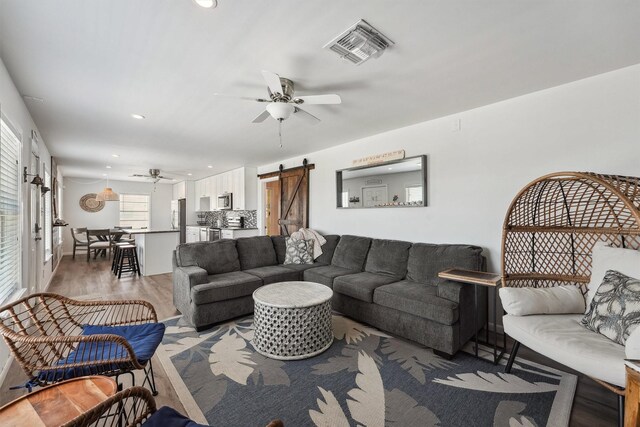 living room featuring a barn door, recessed lighting, visible vents, a ceiling fan, and light wood-style flooring