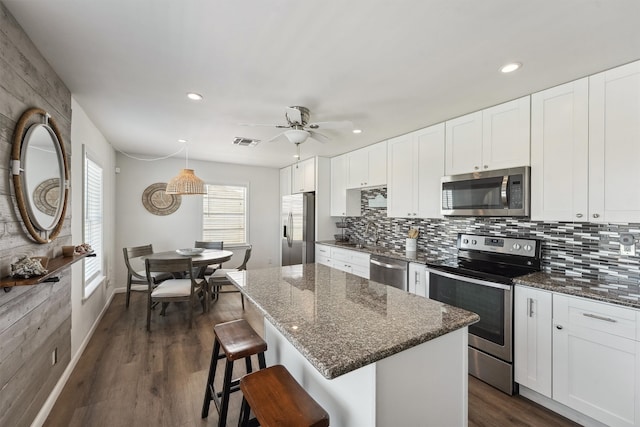 kitchen with a kitchen island, stainless steel appliances, dark stone counters, white cabinets, and dark hardwood / wood-style flooring