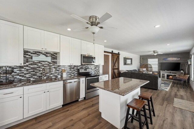 kitchen with stainless steel appliances, a sink, a barn door, ceiling fan, and a breakfast bar