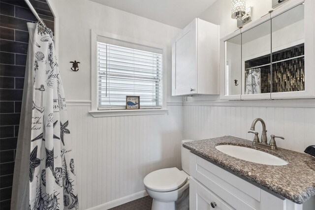 bathroom with tiled shower, a wainscoted wall, vanity, and toilet