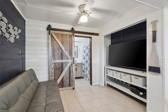 tiled living room featuring a barn door, wooden walls, and ceiling fan