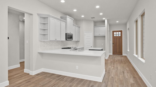 kitchen with sink, kitchen peninsula, white cabinetry, and light hardwood / wood-style flooring