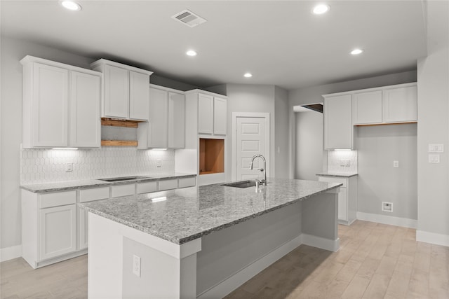 kitchen featuring white cabinetry, sink, and an island with sink