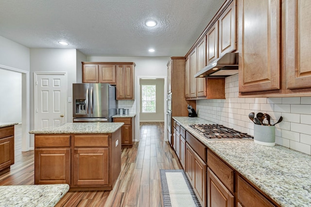 kitchen featuring a kitchen island, a textured ceiling, light hardwood / wood-style floors, stainless steel appliances, and ventilation hood