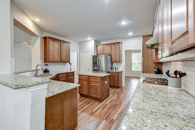 kitchen featuring appliances with stainless steel finishes, sink, kitchen peninsula, light stone counters, and extractor fan