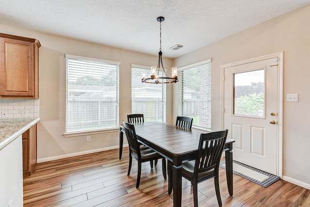 dining area with a chandelier, a textured ceiling, and light wood-type flooring