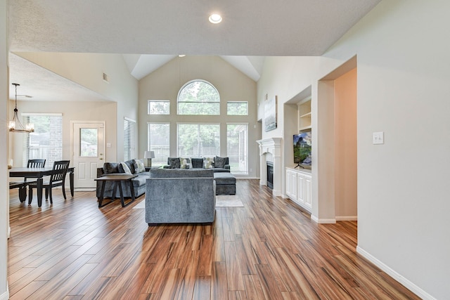 living room featuring high vaulted ceiling, hardwood / wood-style floors, a textured ceiling, and an inviting chandelier