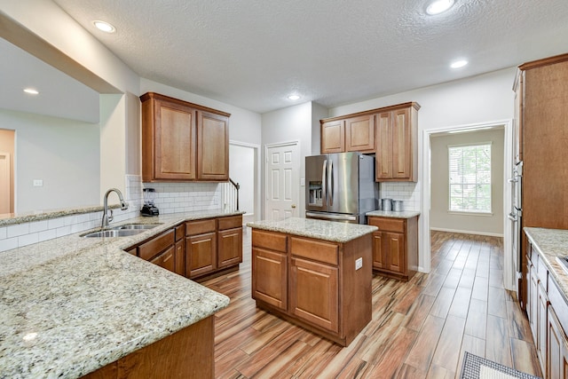 kitchen with sink, light stone countertops, a center island, appliances with stainless steel finishes, and a textured ceiling