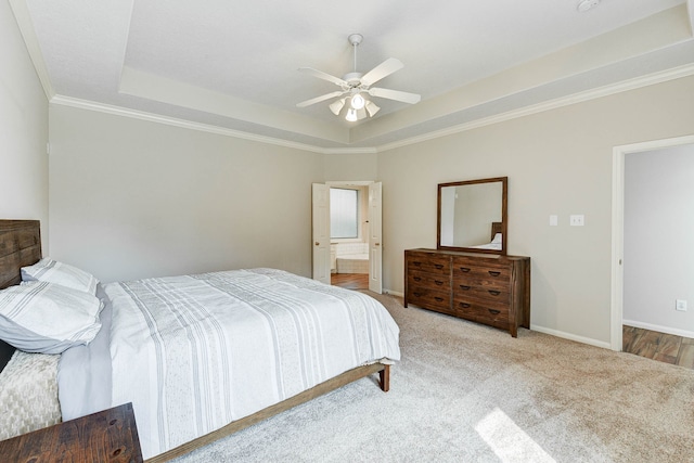 bedroom featuring a tray ceiling, ensuite bath, ornamental molding, light colored carpet, and ceiling fan