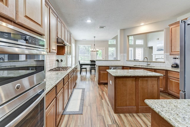 kitchen featuring sink, a textured ceiling, a center island, stainless steel appliances, and decorative light fixtures