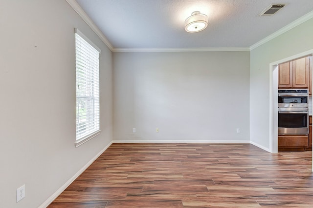 spare room with a textured ceiling, crown molding, wood-type flooring, and plenty of natural light