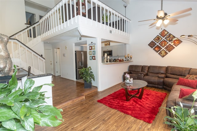 living room with a towering ceiling, ceiling fan, and dark hardwood / wood-style flooring