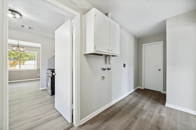 laundry area with hookup for a washing machine, light hardwood / wood-style floors, cabinets, and a chandelier