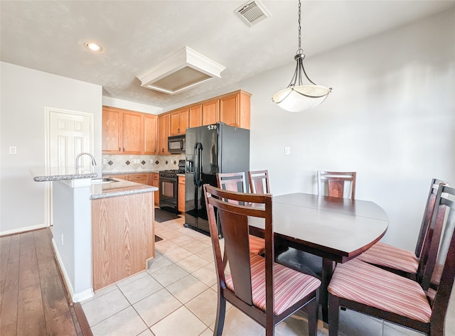 kitchen with light stone countertops, black appliances, light wood-type flooring, backsplash, and hanging light fixtures