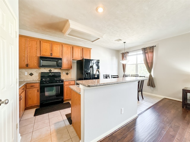 kitchen with a kitchen island, light hardwood / wood-style flooring, black appliances, light stone countertops, and pendant lighting