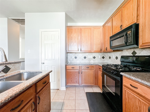 kitchen with decorative backsplash, light stone counters, light tile patterned floors, black appliances, and sink