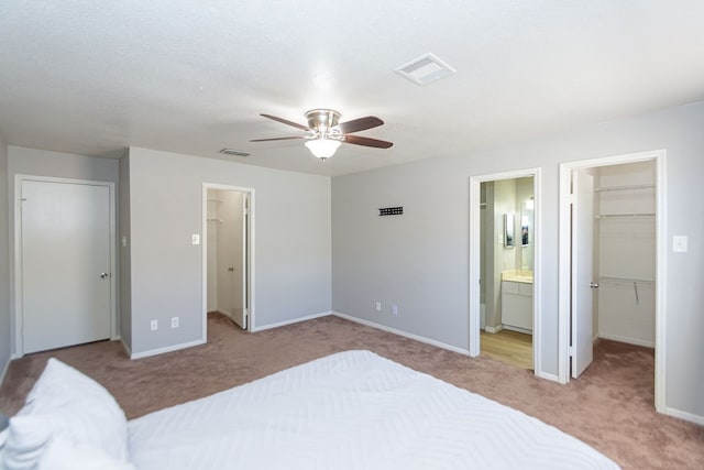 carpeted bedroom with a spacious closet, ensuite bathroom, a closet, and ceiling fan