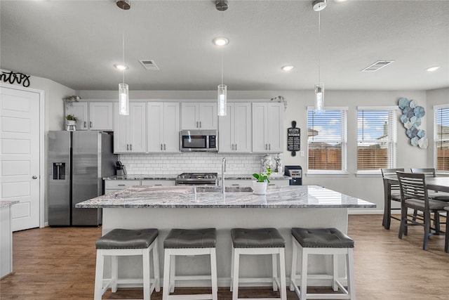 kitchen with tasteful backsplash, sink, an island with sink, stainless steel appliances, and white cabinets