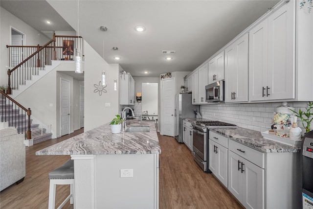 kitchen featuring hanging light fixtures, wood-type flooring, sink, white cabinets, and appliances with stainless steel finishes