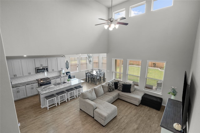 living room with a towering ceiling, light hardwood / wood-style flooring, sink, and ceiling fan