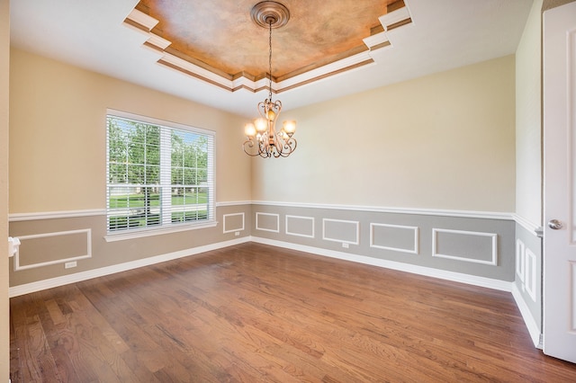 empty room featuring hardwood / wood-style floors, an inviting chandelier, and a raised ceiling