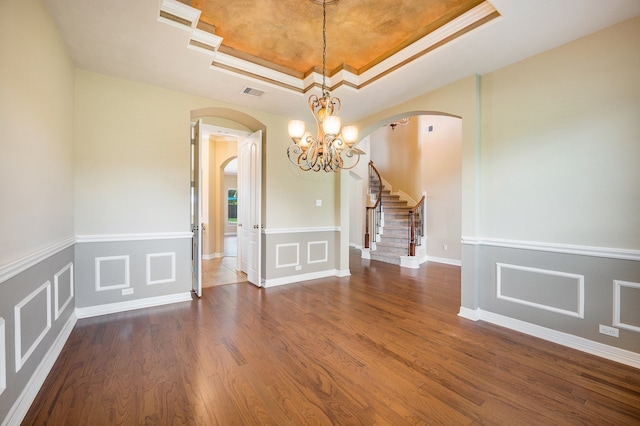 unfurnished dining area featuring an inviting chandelier, crown molding, a tray ceiling, and dark hardwood / wood-style flooring