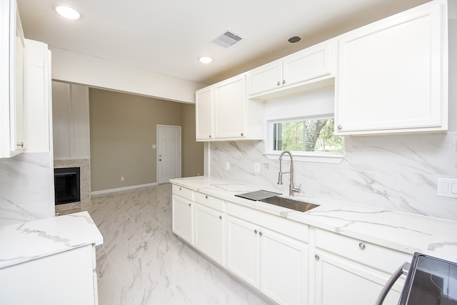 kitchen featuring backsplash, white cabinetry, light stone countertops, and sink