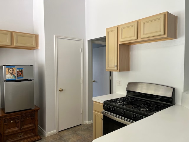 kitchen with stainless steel fridge, light tile patterned floors, light brown cabinetry, and range with gas cooktop