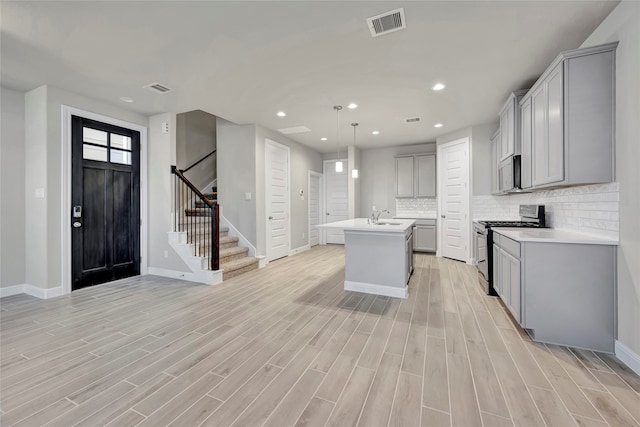 kitchen featuring stainless steel appliances, light wood-type flooring, a center island with sink, and gray cabinets