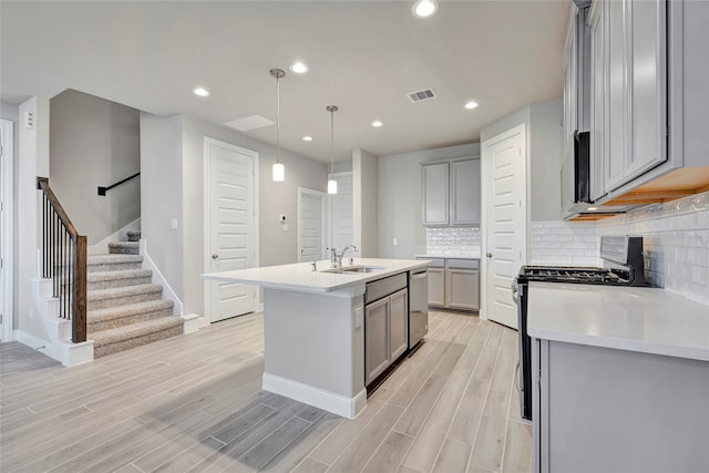 kitchen with an island with sink, light hardwood / wood-style flooring, gas range oven, gray cabinets, and decorative light fixtures