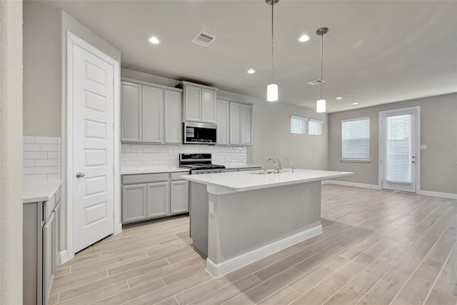 kitchen with light wood-type flooring, sink, pendant lighting, gray cabinets, and stainless steel appliances