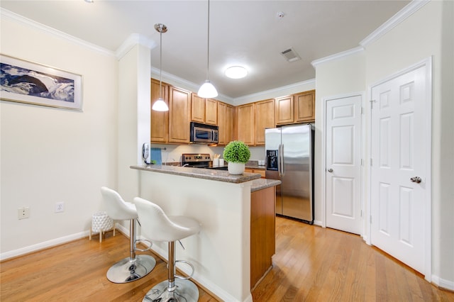 kitchen with a breakfast bar area, kitchen peninsula, pendant lighting, appliances with stainless steel finishes, and light hardwood / wood-style floors