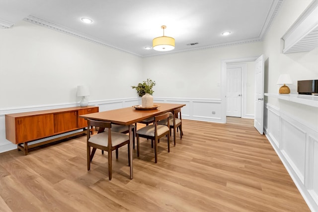 dining room featuring crown molding, light wood-style floors, wainscoting, and a decorative wall