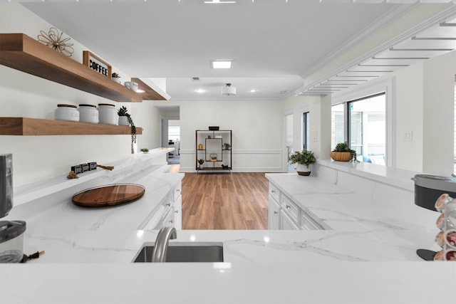 kitchen with crown molding, open shelves, light stone countertops, white cabinets, and a sink