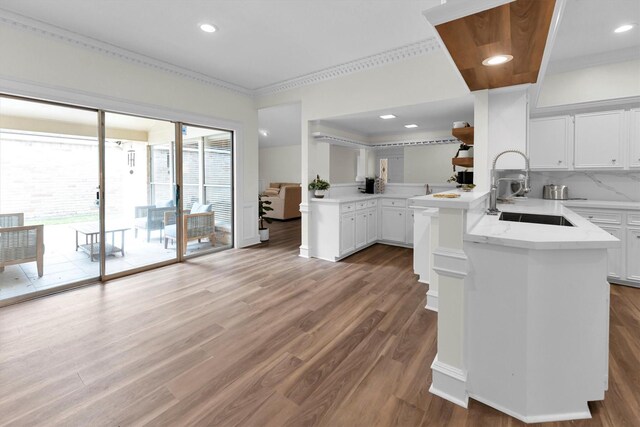 kitchen with a sink, white cabinets, a peninsula, and wood finished floors