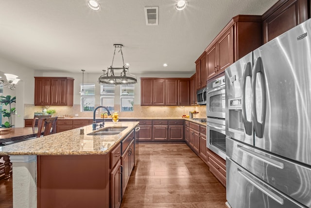 kitchen featuring dark hardwood / wood-style floors, stainless steel appliances, a center island with sink, sink, and decorative light fixtures