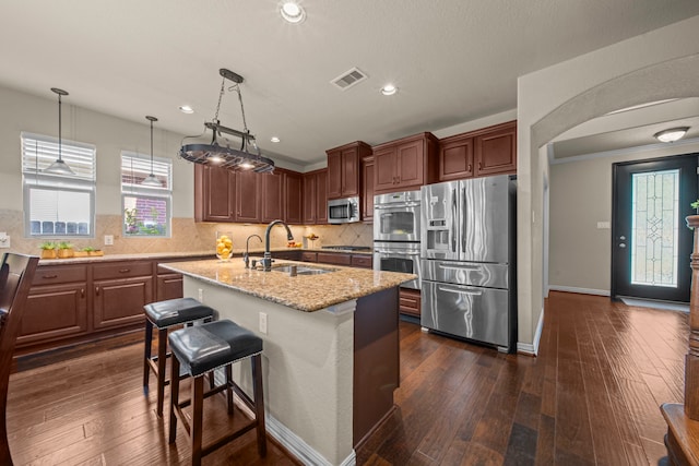 kitchen with appliances with stainless steel finishes, a kitchen island with sink, sink, and dark wood-type flooring