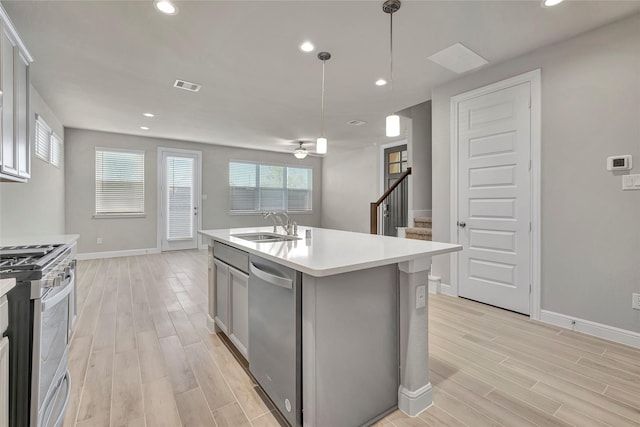 kitchen with sink, a kitchen island with sink, stainless steel appliances, white cabinets, and decorative light fixtures